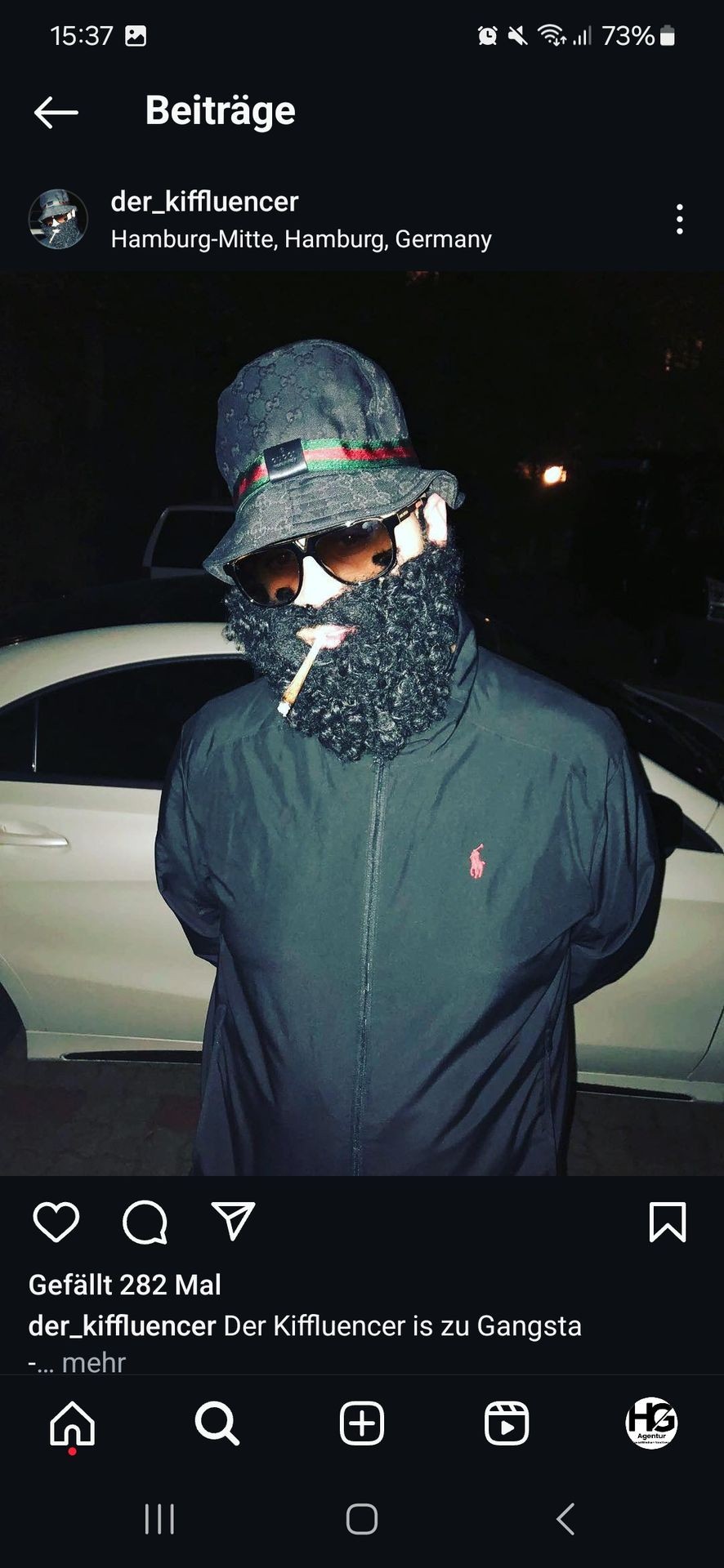 Person in dark clothing and a hat standing in front of a white car at night.